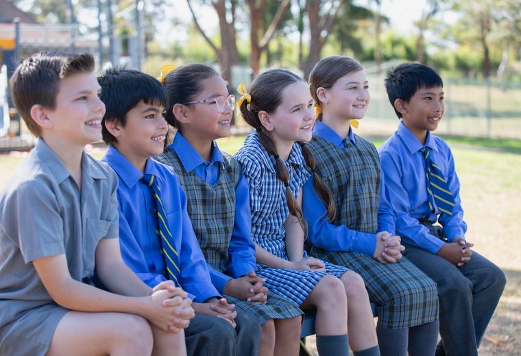 Group of primary school students sitting on bench outdoors.