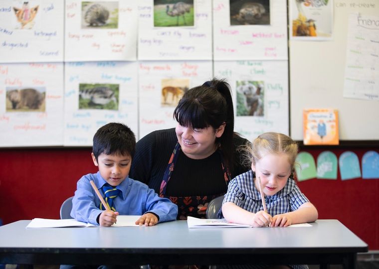 Primary school students doing school work at desk with teacher.