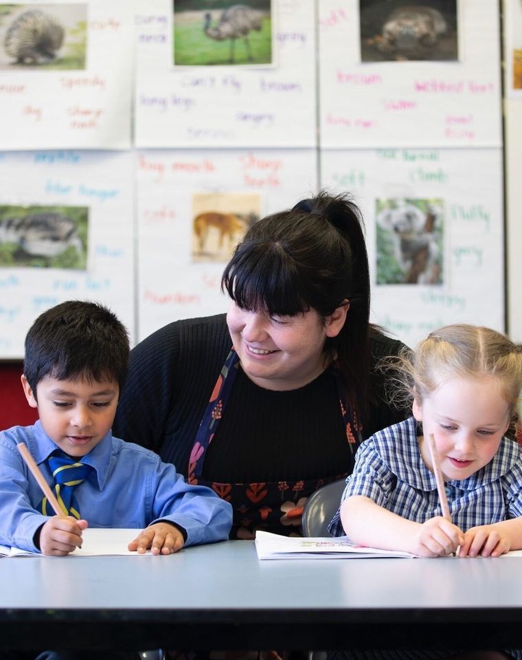 Primary school students doing school work at desk with teacher.