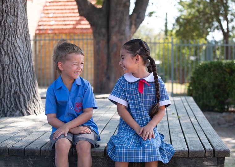 Two primary school students sitting under tree outdoors.