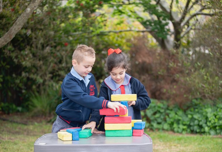 Primary school students playing with colourful blocks outdoors.