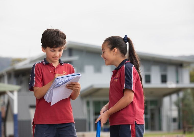 Primary school students outdoors with notebook.