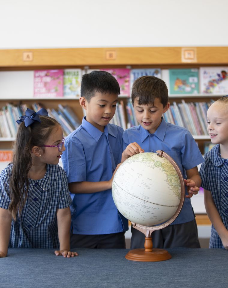 Primary school students looking at globe in library.