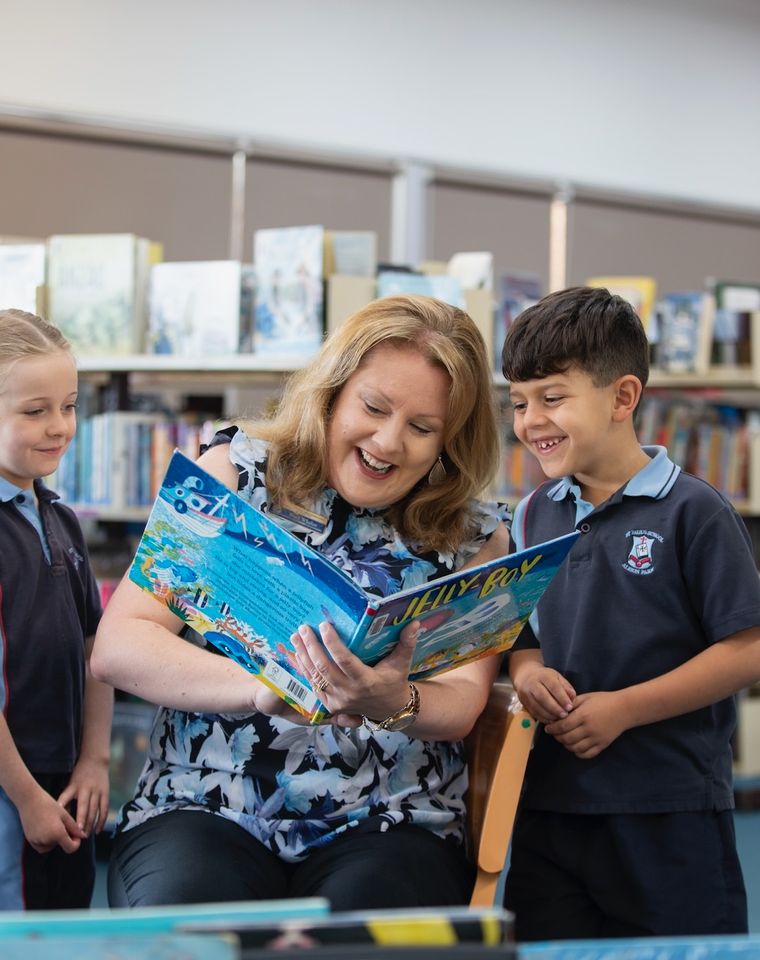 Primary school students reading a book in library with teacher.