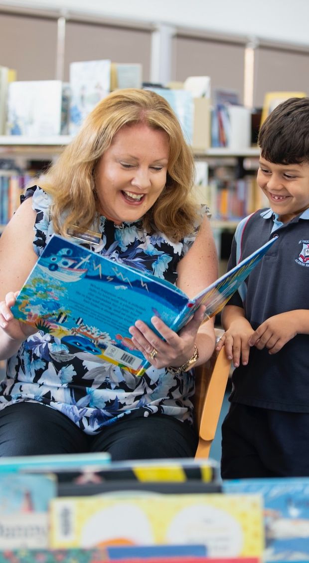 Primary school students reading a book in library with teacher.