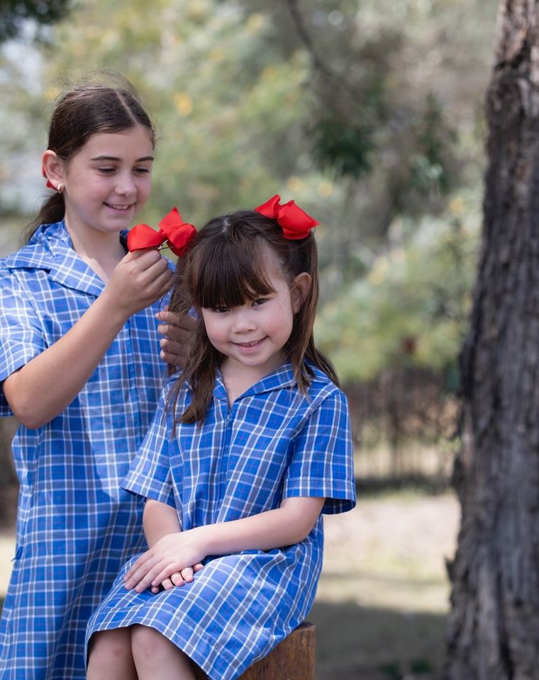 Primary school students standing under tree outdoors.