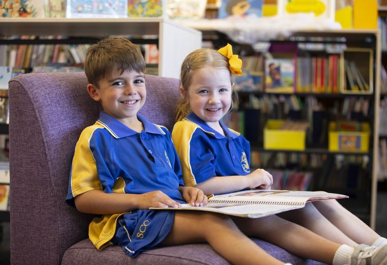 Primary school students reading book in library.