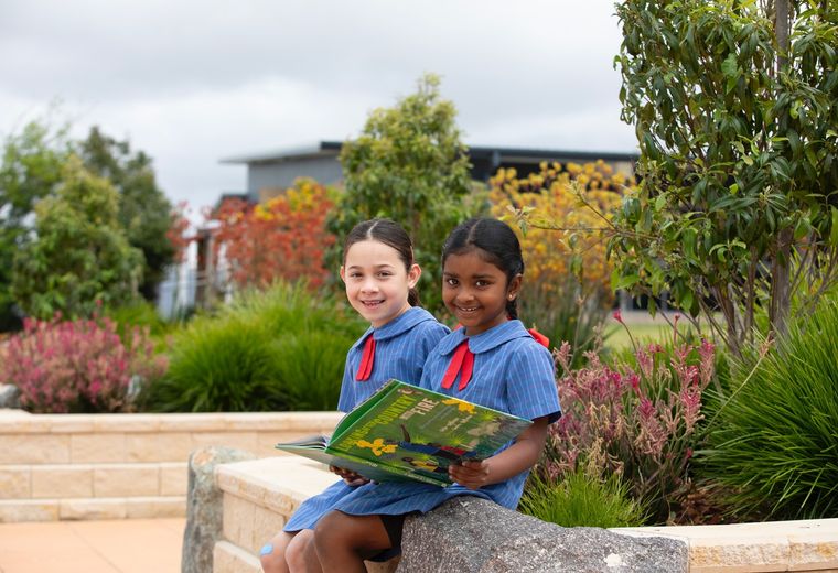 Primary school students smiling at camera while reading a book in garden.