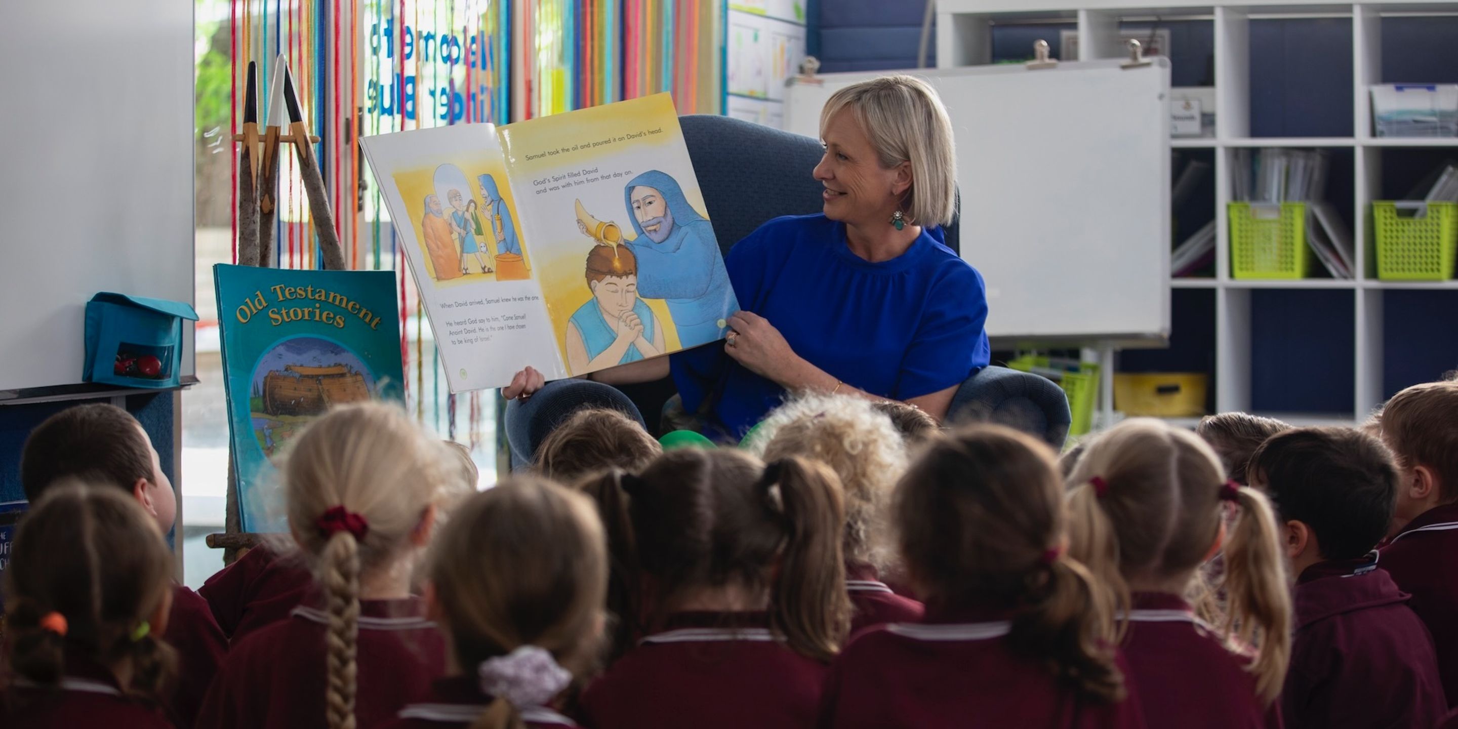 Primary school students listening to teacher read a book in classroom.