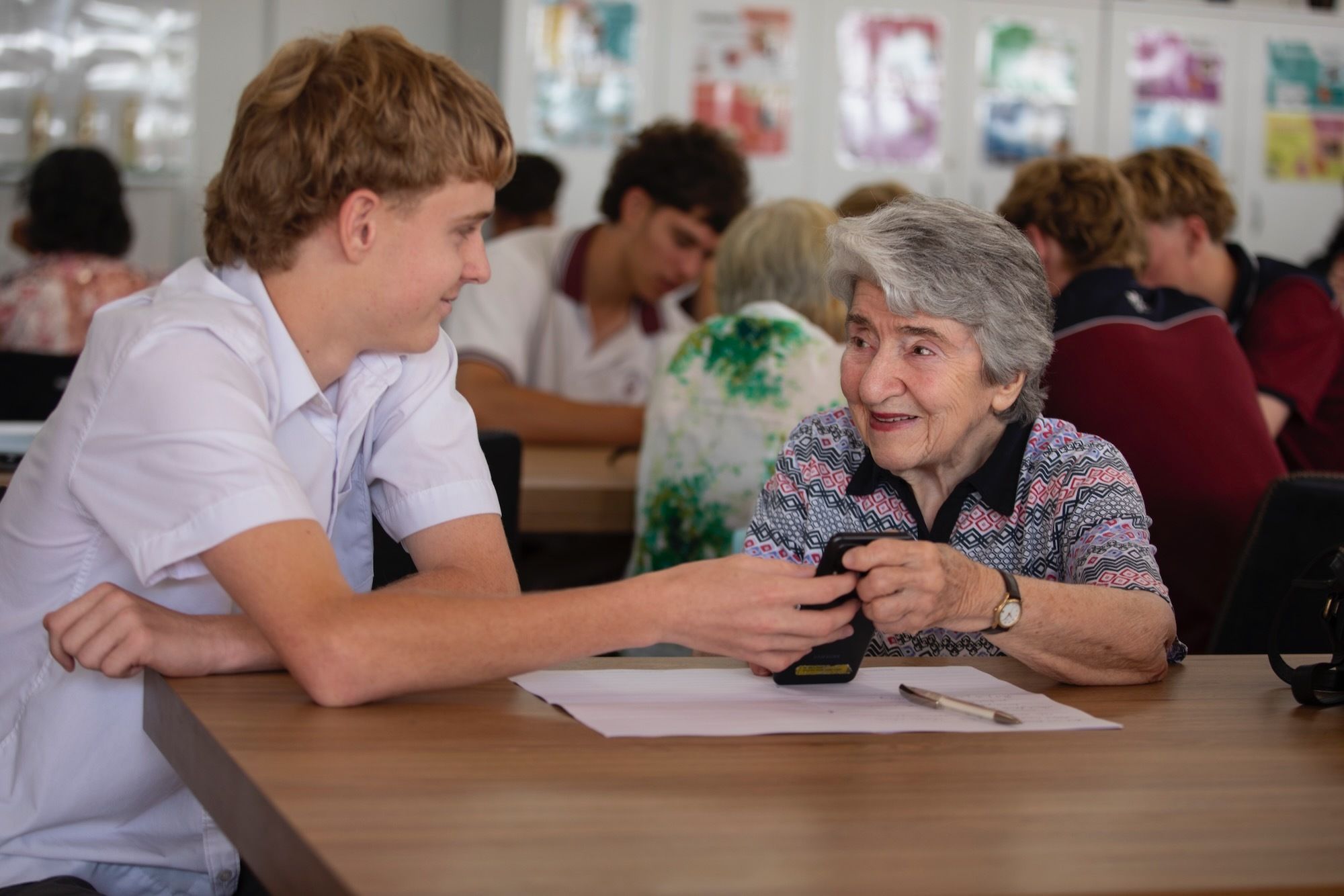 High school student helping elderly person with technology.