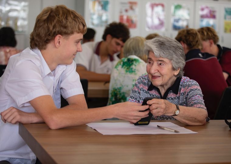 High school student helping elderly person with technology.