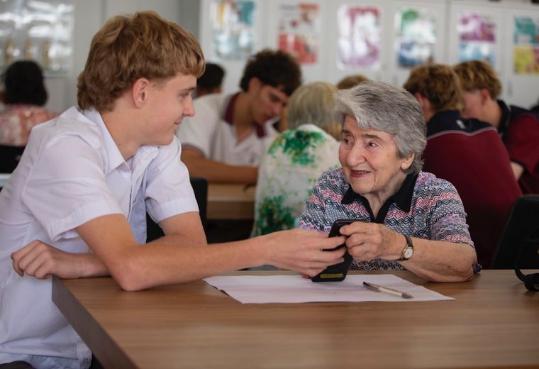 High school student helping elderly person with technology.