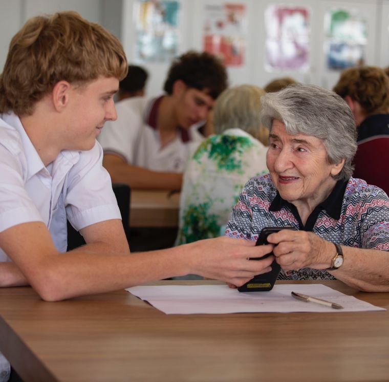 High school student helping elderly person with technology.