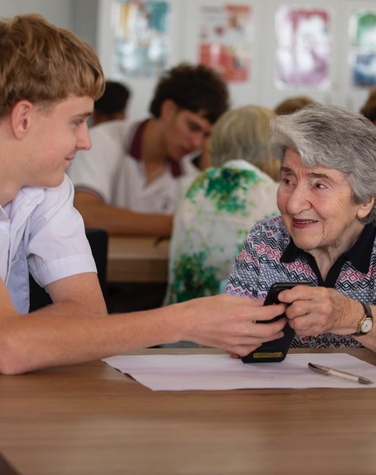 High school student helping elderly person with technology.