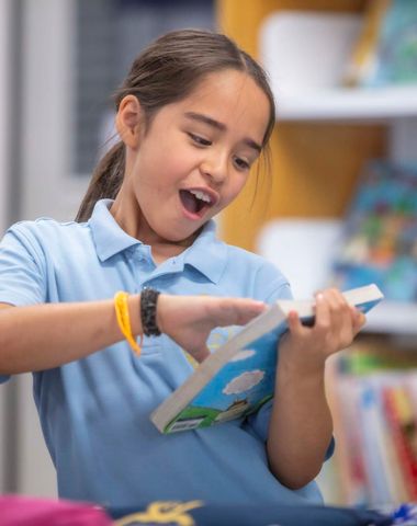 A Junior School student laughing and reading in the Library at Ruyton Girls' School