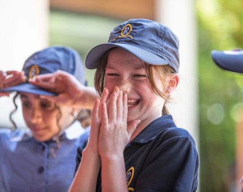 A Junior School student from Ruyton Girls' School laughing with her friends. She is wearing PE uniform in House colours.