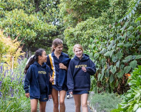 Senior School students smiling at each other as they walk down a garden path.