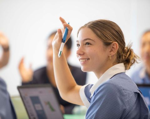 A Senior School student with her hand up in class