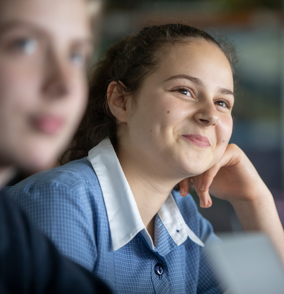 Student leaning on her hand, smiling up at the teacher in class.