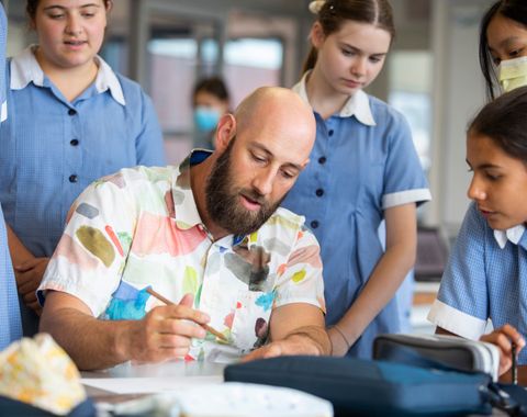 Male Art Teacher drawing while Ruyton students watch over his shoulder.