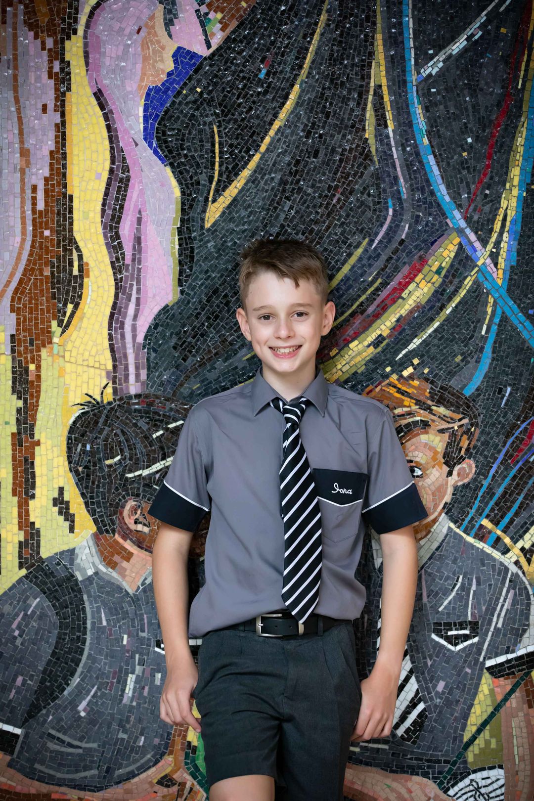 Single Iona students standing in from of Iona's tile mural