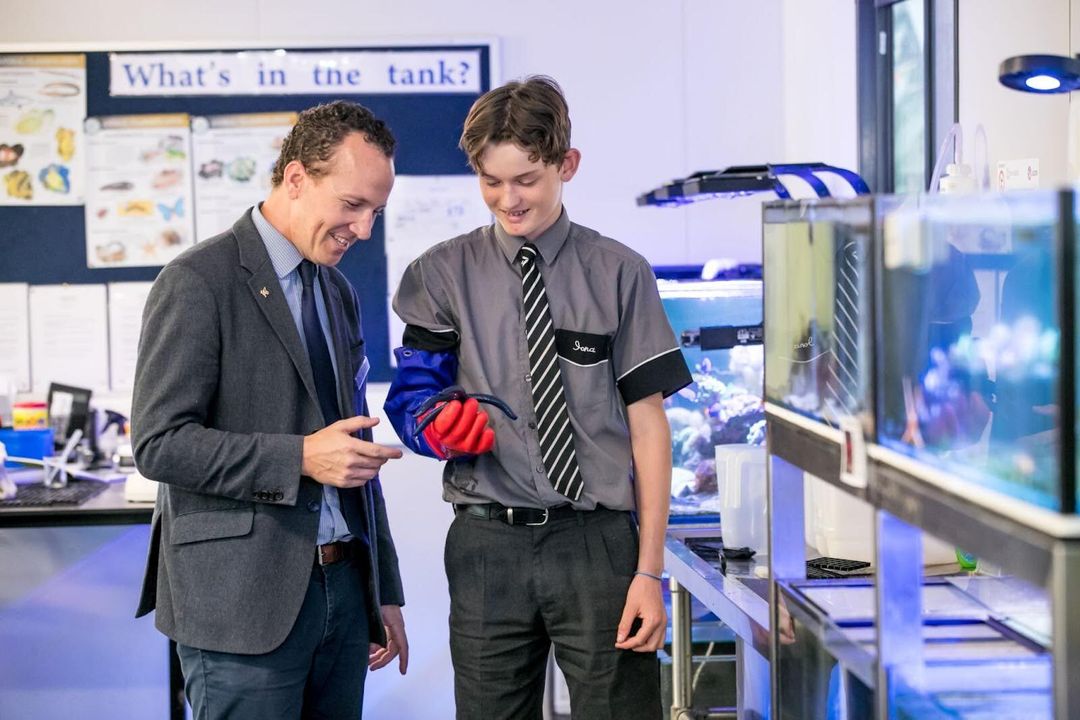 A teacher and student examine a specimen in the student's hand next to fish tanks
