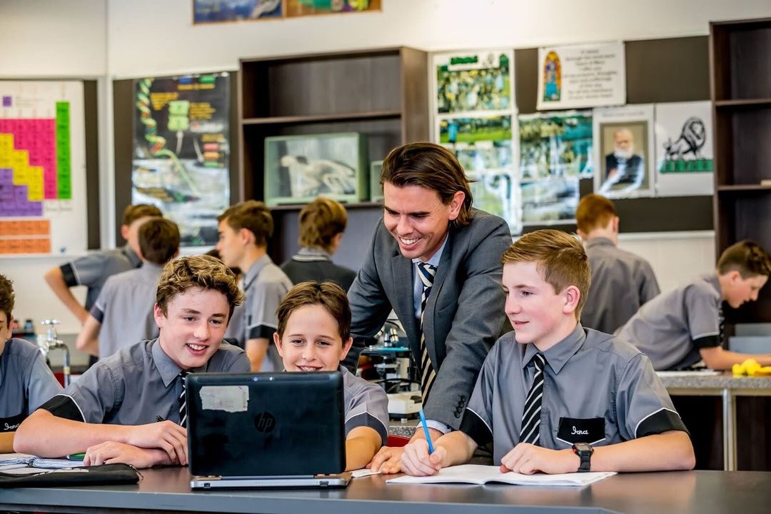 A group of students looking at a laptop screen with a teacher leaning over them