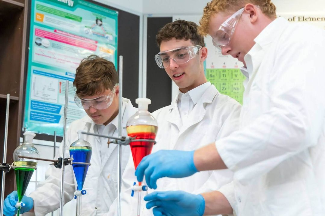A group of three students in lab coats with various chemistry apparatus