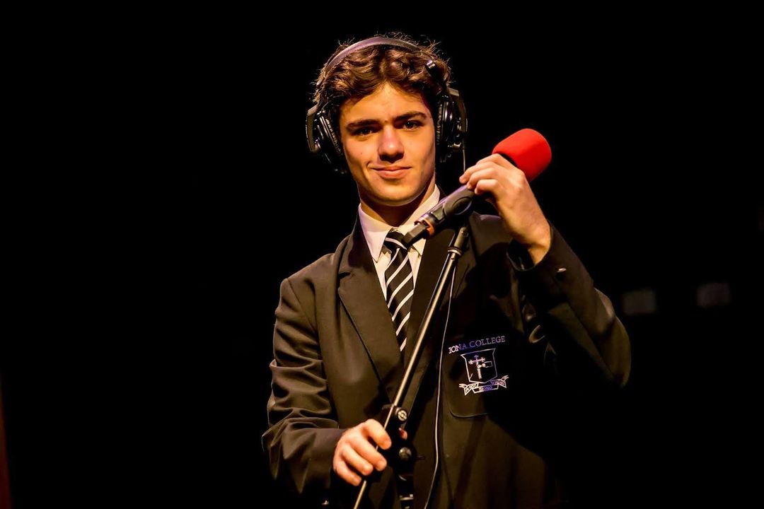 Single students with headphones on next to a microphone with a black background