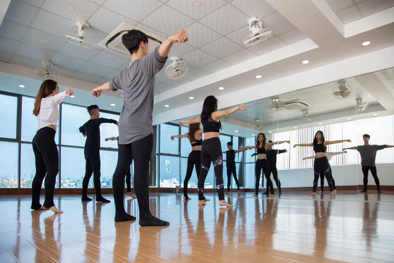 Group of dancers standing at big window in studio and repeating movement after front woman