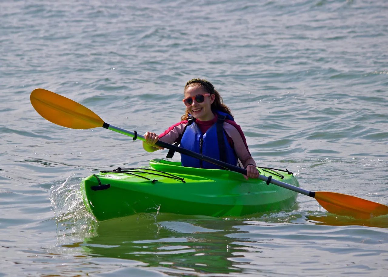 A teen girl paddles a kayak on the calm waters of Casco Bay, Maine.