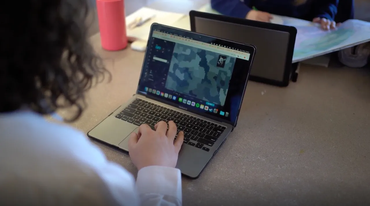 Photo taken over the shoulder of an upper secondary school-aged student from Overnewton Anglican Community College who is using a laptop to view curriculum-based content for their Visual Arts class.