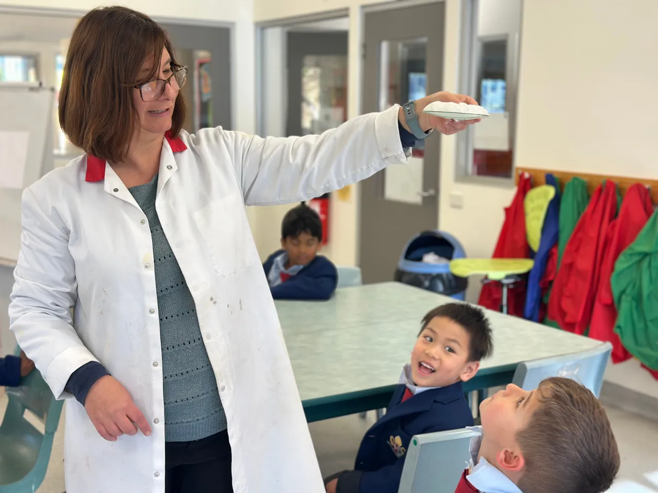 Lower primary school aged students from Overnewton Anglican Community College Junior School marvelling at a Lab Technician conducting an awe-inspiring experiment as part of 2025 National Science Week.