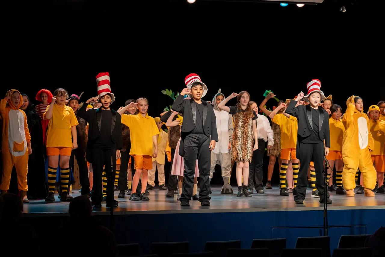 A large group of upper primary school aged students in bright costumes performing on stage as part of the cast of the Middle School Year 5 & 6 Musical Season 1 production of Seussical KIDS.