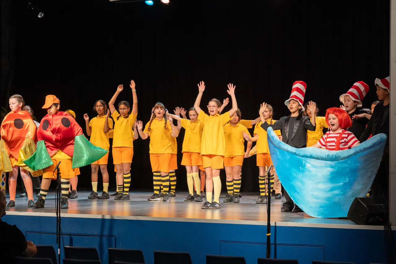A large group of upper primary school aged students in bright costumes performing on stage as part of the cast of the Middle School Year 5 & 6 Musical Season 1 production of Seussical KIDS.