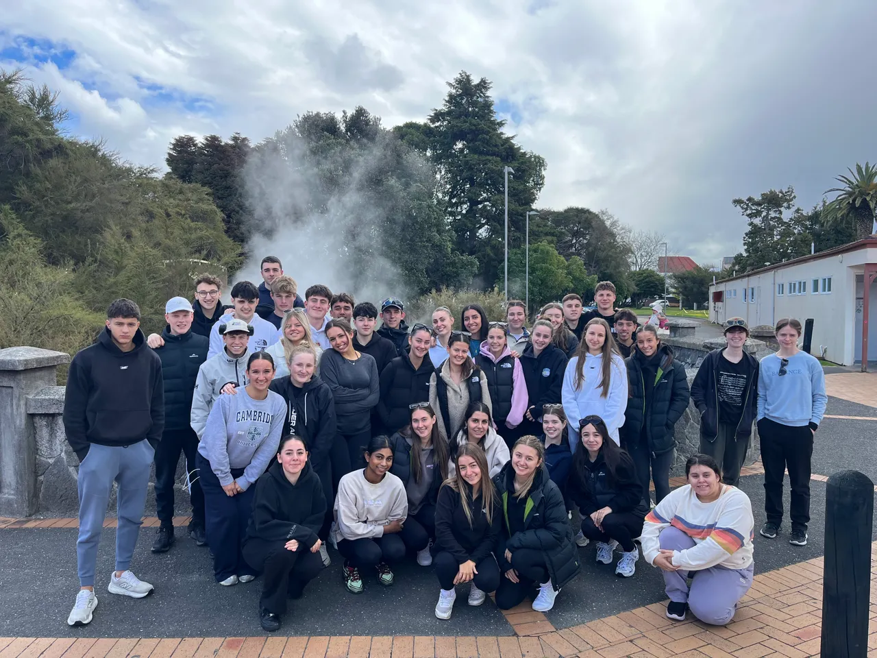 Overnewton upper secondary school-aged students standing in front of a steaming geothermal spring in Rotorua, New Zealand, during the annual Year 11 Co Curricular educational travel program.