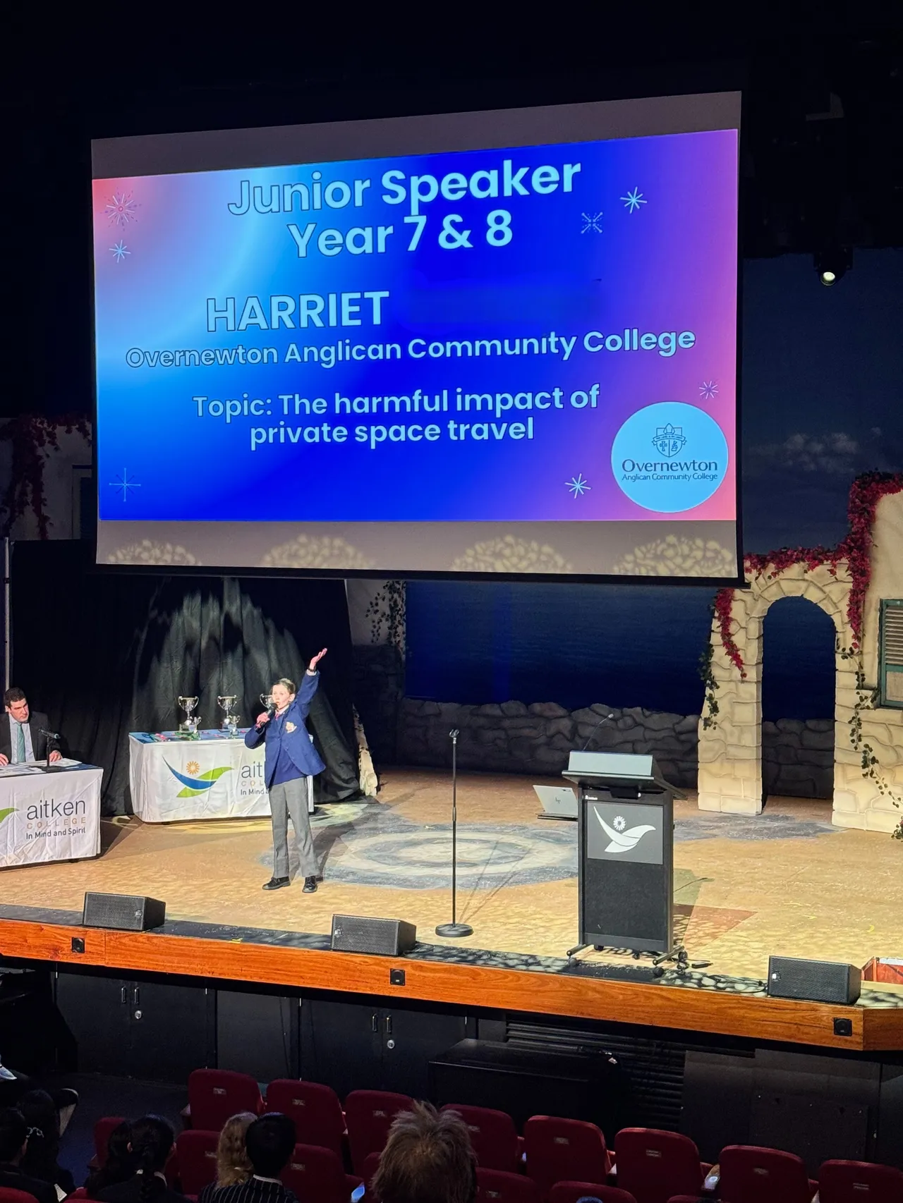 Photo of lower secondary school-aged student Harriet speaking on stage proudly representing Overnewton, delivering her winning speech at the 2025 ACS Public Speaking Championships.