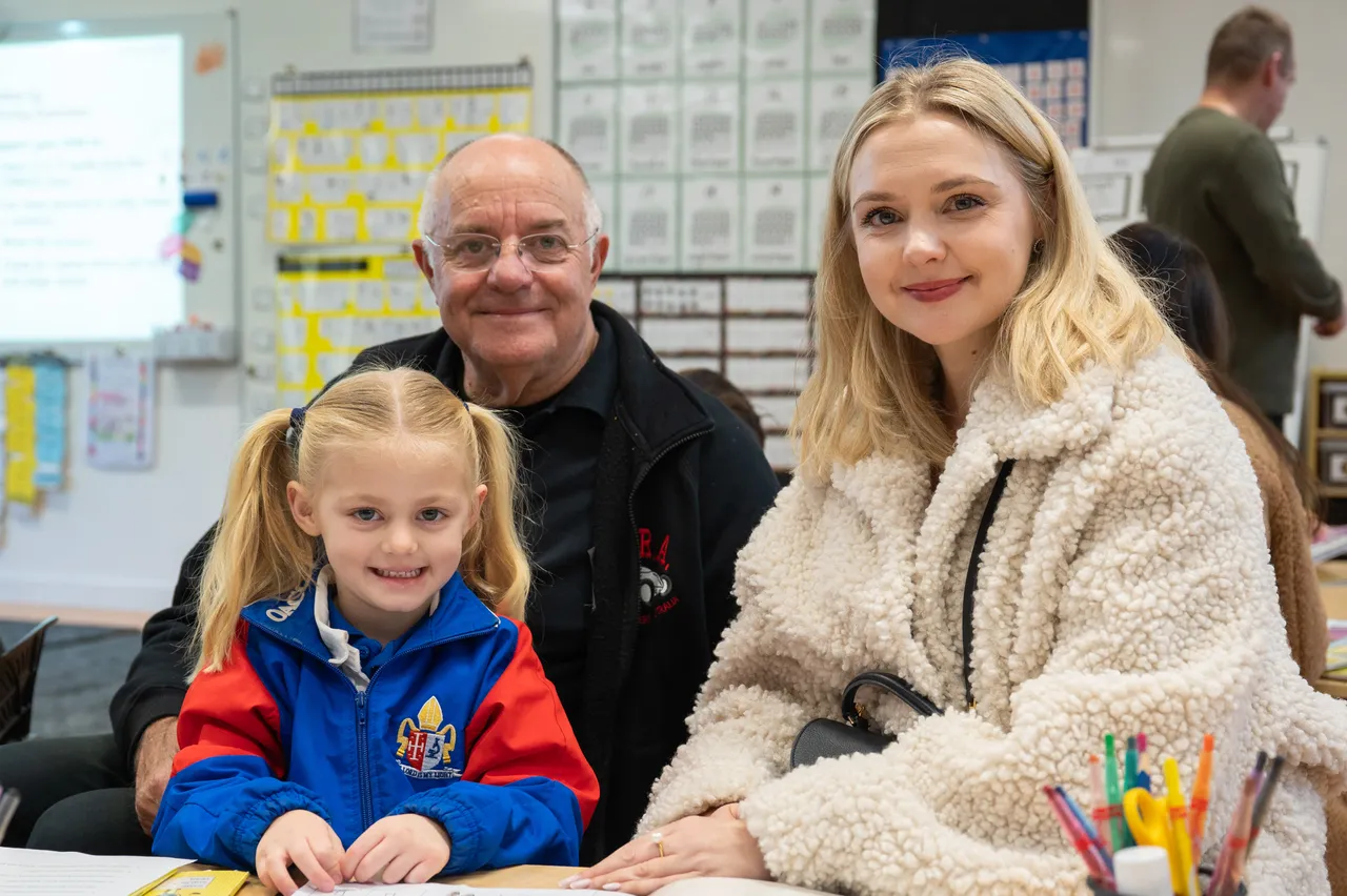 Lower primary school aged student proudly posing with her mother and grandfather during the Junior School Celebration of Learning event.