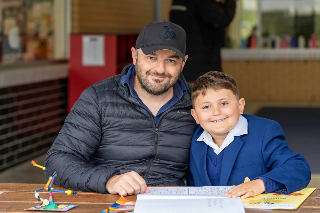 Lower primary school aged student speaking with his father, a guest at Overnewton Junior School during the Celebration of Learning event.