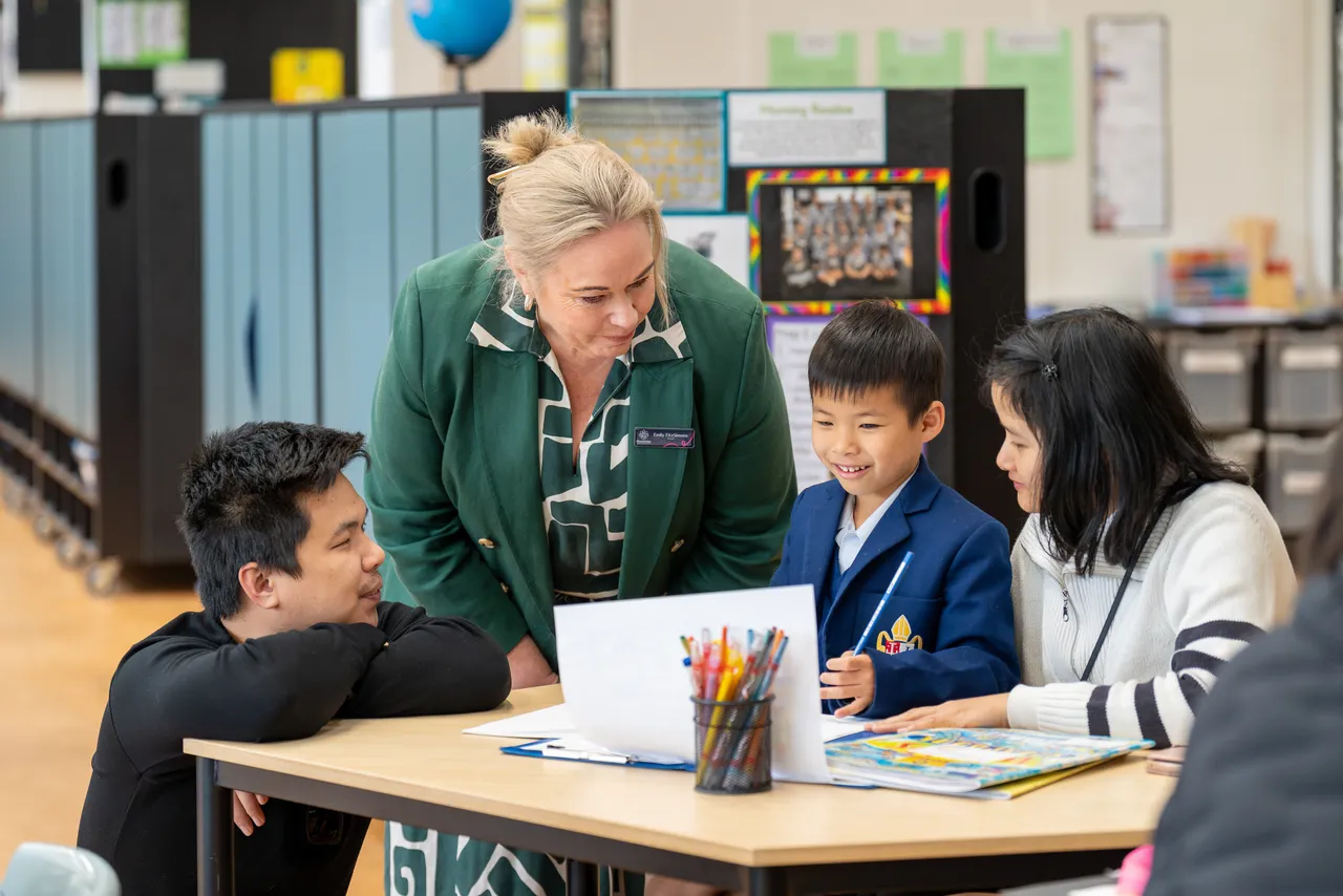 Lower primary school aged student presenting his work to Principal Emily FitzSimons and his parents who are guests at Overnewton Junior School during the Celebration of Learning event.