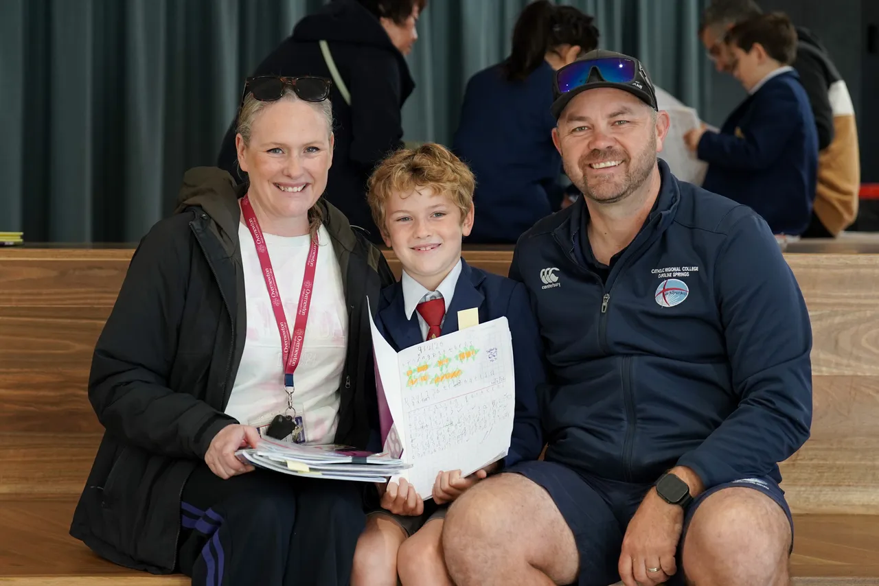 Lower primary school aged student, smiling with his parents who are guests at Overnewton's Junior School during the 2026 Celebration of Learning event.