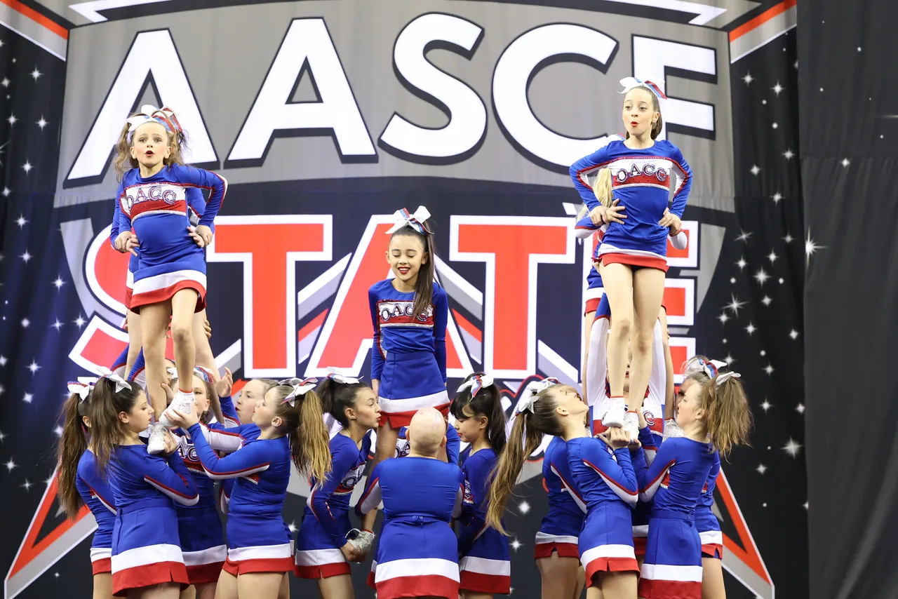 Lower secondary school aged students from Overnewton's Middle School Cheer team performing a technical acrobatic formation as part of their prize-winning routine on stage at the 2025 AASCF State Championships.