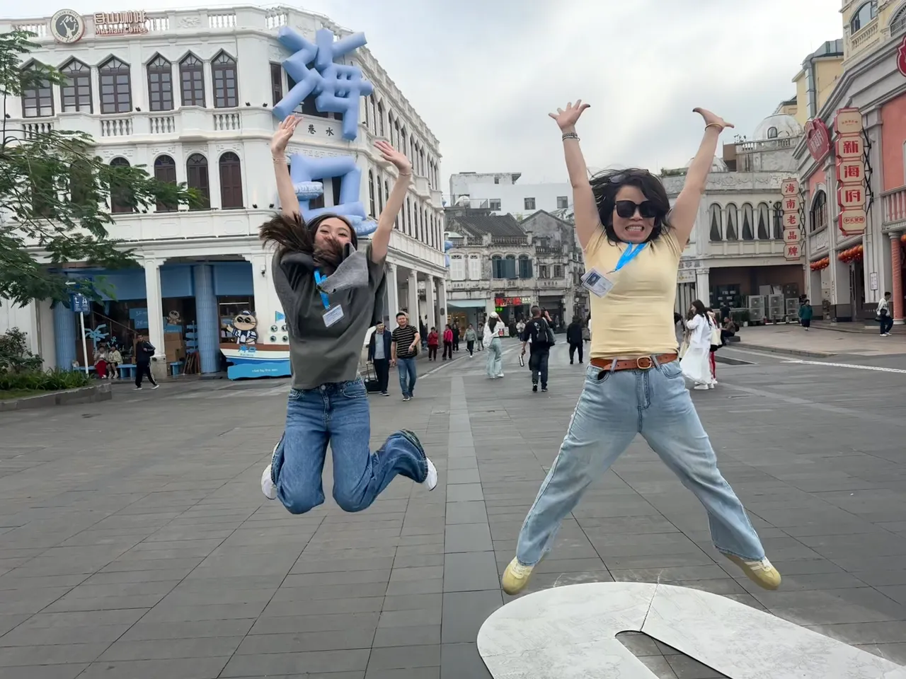 Student and staff member shown jumping in mid air in front of a building in the shopping district of Hainan as part of Overnewton's 2025 educational travel tour to China.