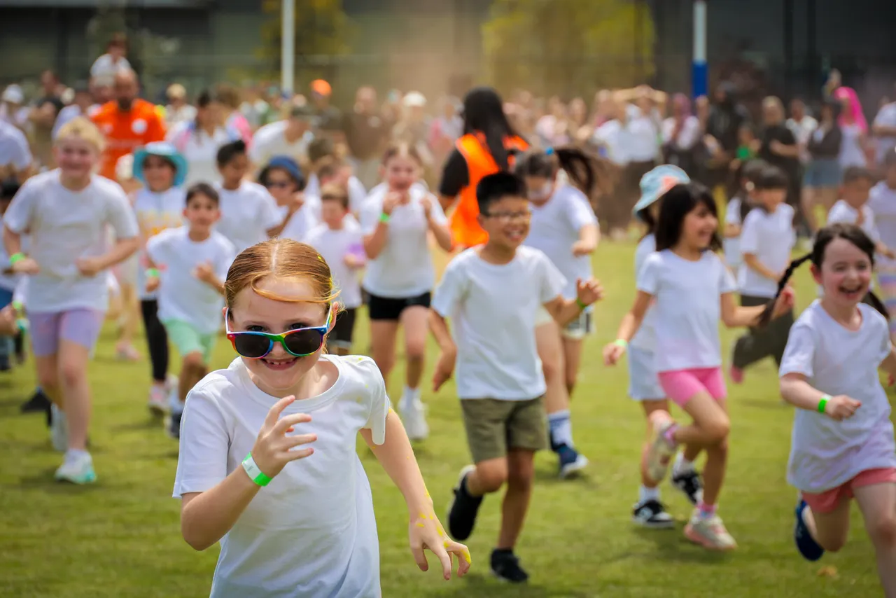 Overnewton a mass of primary school-aged children running towards the camera at bi annual Parents and Friends Association fundraising Colour Fun Run held at Canowindra Campus Oval, Taylors Lakes.