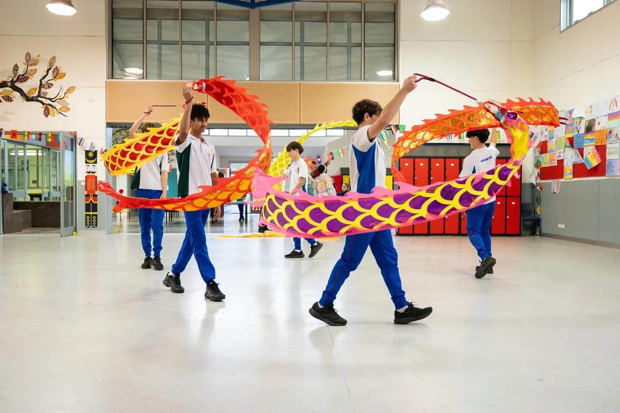 A group of middle secondary school-aged students from Year 9 walking in a circle, swinging a colourful dragon puppet in the air during Overnewton's 2025 Languages and Culture Week.