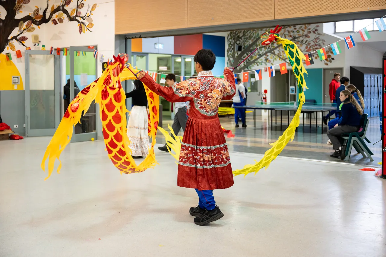 A middle secondary school-aged students from Year 9 in traditional Chinese dress swinging a colourful dragon puppet in the air during Overnewton's 2025 Languages and Culture Week.
