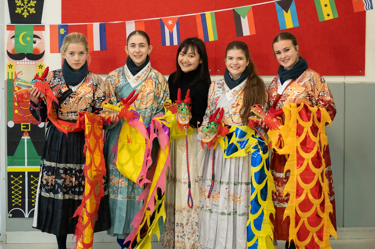 A group of middle secondary school-aged students from Year 9 in traditional Chinese dress flanking College Head of Languages, Sunny Huang, and holding dragon puppets during Overnewton's 2025 Languages and Culture Week.