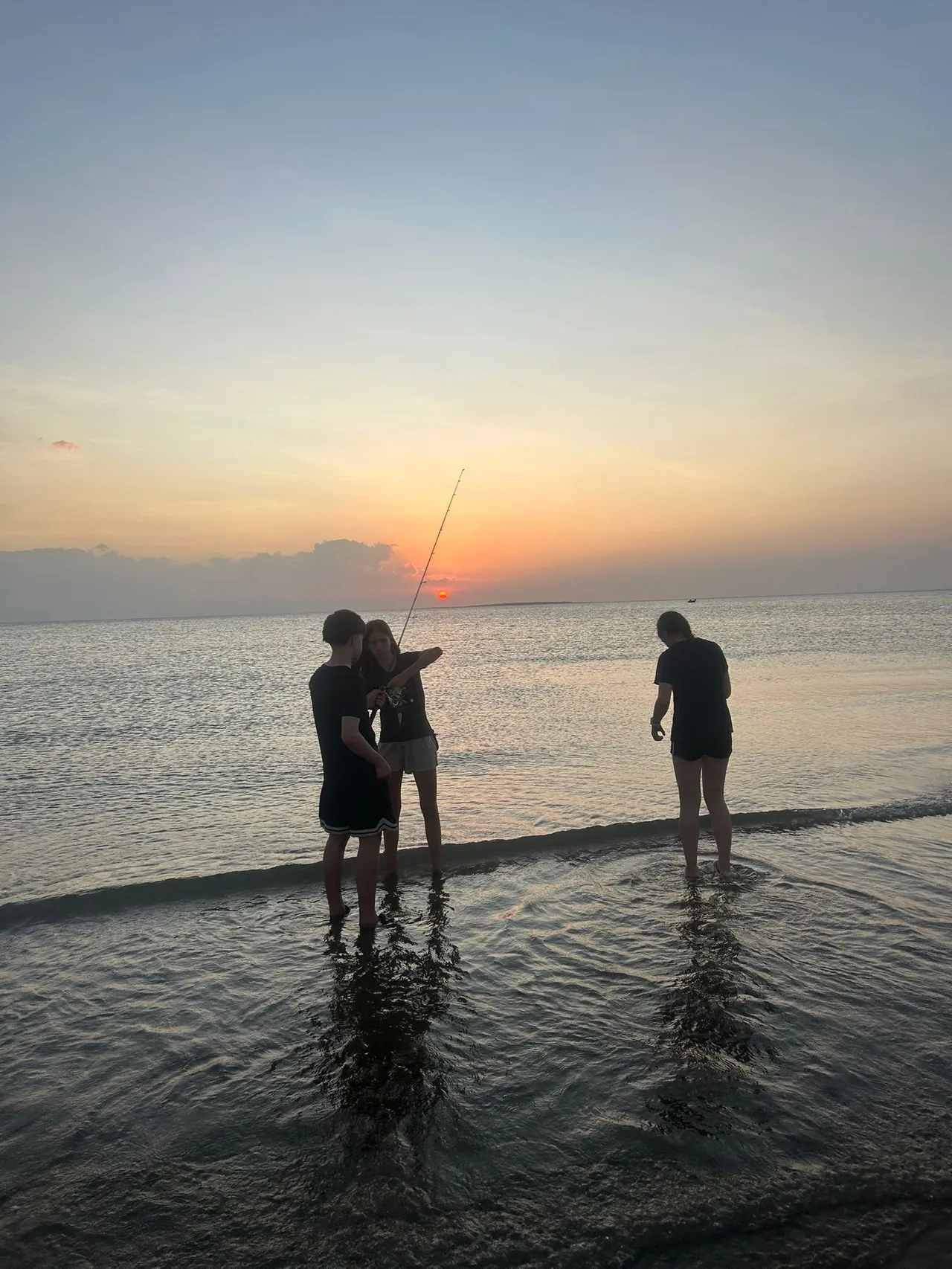 A silhoutte of three students standing at the water's edge, readying a large fishing rod, on a sunset-lit beach at Elcho Island in the Northern Territory during Overnewton’s 2025 Galiwin’ku educational travel program.