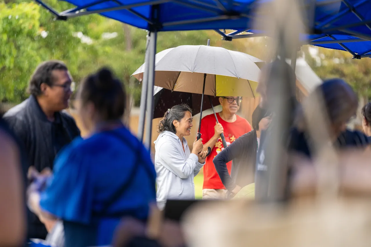 Members of the Overnewton community sheltering under a large umbrella at the sausage sizzle during the inaugural Canowindra Parent Information Evening.