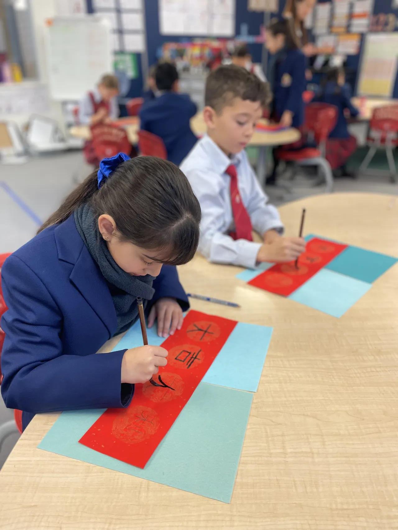 Middle primary school aged students from Overnewton Junior School using traditional brushes to paint Chinese characters on red banners during Overnewton’s 2025 Languages and Culture Week.